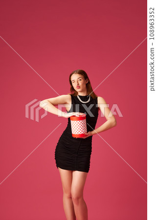 Happy young girl in elegant black dress holding present, celebrating against pink studio background. Christmas time Happy young girl in elegant black dress holding present, celebrating against pink studio background. Christmas time 108963352