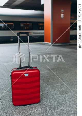 Forgotten travel bag on the train station. Red suitcase on empty station platform. Travel and vacation theme background. Travel banner Forgotten travel bag on the train station. Red suitcase on empty station platform. Travel and vacation theme background. Travel banner 108964093