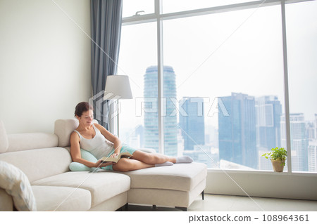 Woman reading a book at big window with city view 108964361