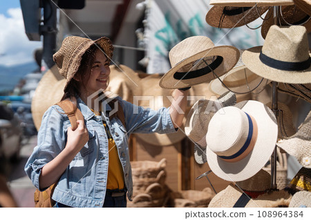 Happy young woman asian is visit local market during her trip and purchase straw hat handmade. Tourist women travel in Chiang mai enjoy shopping market during holidays, backpacker traveller Happy young woman asian is visit local market during her trip and purchase straw hat handmade. Tourist women travel in Chiang mai enjoy shopping market during holidays, backpacker traveller 108964384