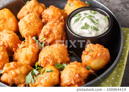 Southern Hush Puppies are light and flakey cornmeal dough that is fried golden brown on the outside and soft on the inside closeup on the plate. Horizontal 108964419