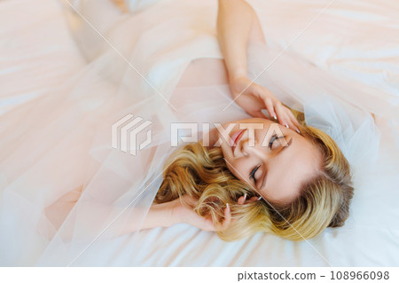 Morning of the bride. Delicate and beautiful blonde bride in bed under veil. 108966098