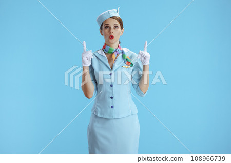 surprised female stewardess on blue pointing up at copy space 108966739