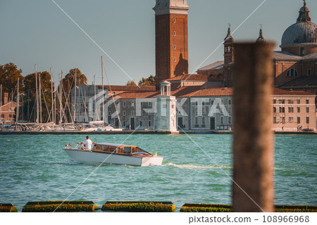 White boat in the water with a clock tower in the heart of Venice. Iconic city known for canals, bridges, and waterways. White boat in the water with a clock tower in the heart of Venice. Iconic city known for canals, bridges, and waterways. 108966968