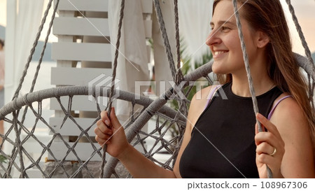 Smiling female tourist enjoying sea breeze while swinging on the beach at sunset. Concept of summertime, vacation and beach holidays. Smiling female tourist enjoying sea breeze while swinging on the beach at sunset. Concept of summertime, vacation and beach holidays. 108967306