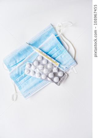 Preparation for vaccination against covid-19. Thermometer, pills, medical mask on a white table. Place for an inscription, vertical photo. 108967455