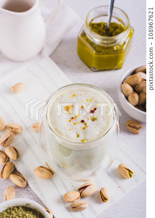 Pistachio matcha latte in a cup and nuts in a bowl and on the table vertical view 108967621
