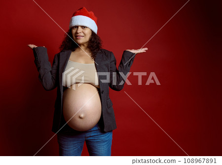 Charismatic pregnant woman, expectant mother in stylish gray blazer and Santa hat, holding copy space on hands palms up Charismatic pregnant woman, expectant mother in stylish gray blazer and Santa hat, holding copy space on hands palms up 108967891