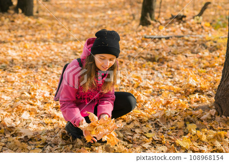 Young woman in a hat collects autumn leaves. Fall season concept. Generation Z and gen z youth Young woman in a hat collects autumn leaves. Fall season concept. Generation Z and gen z youth 108968154