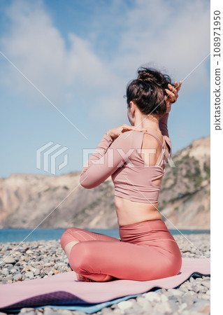Middle aged well looking woman with black hair, fitness instructor in leggings and tops doing stretching and pilates on yoga mat near the sea. Female fitness yoga routine concept. Healthy lifestyle 108971950