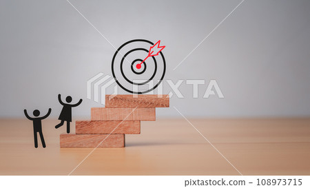 Company employees climb the square wooden steps to reach the dart board. It represents the concept of business strategy and target action plan. 108973715