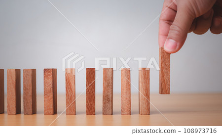 Businessman hand stopping falling blocks on table, stopping the domino effect concept for business solution, strategy and successful intervention. 108973716