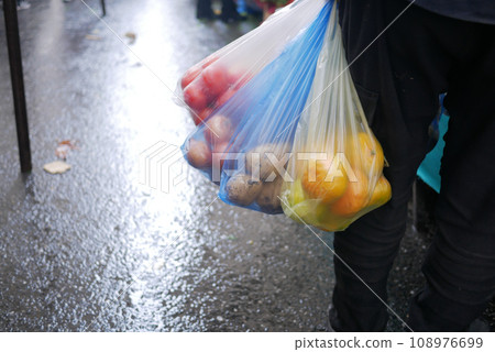A man holds plastic bags in his hand with vegetables A man holds plastic bags in his hand with vegetables 108976699