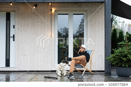 Young man sitting with dog on terrace. 108977864