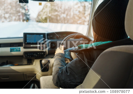Happy Traveler driving car on snowy road, woman Tourist enjoying snow forest view from the car in winter season. Winter travel, Road trip, Exploring and Vacation concepts 108978077
