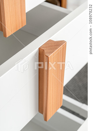 Stylish white office commode with wooden handles and legs with open empty drawers closeup view. Comfortable furniture for home and office furnishing Stylish white office commode with wooden handles and legs with open empty drawers closeup view. Comfortable furniture for home and office furnishing 108978232