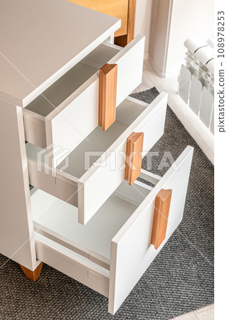 Stylish white office commode with wooden handles and legs with open empty drawers closeup view. Comfortable furniture for home and office furnishing 108978253