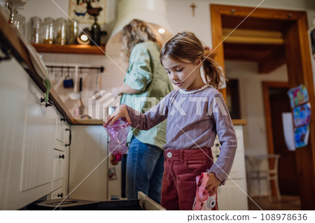 Girl throwing plastic bottles into recycling bin. Daughter sorting the waste according to material into colored bins. 108978636