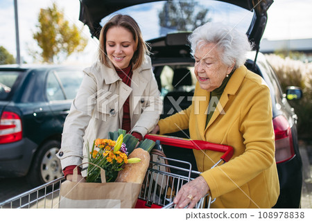 Mature granddaughter helping grandmother load groceries in to the car. Senior woman shopping at the shopping center. 108978838