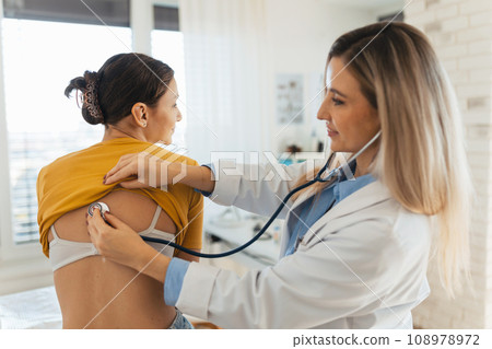 Doctor listening girl's breathing, heartbeats using a stethoscope. Teenage girl visiting paediatrician for annual preventive physical examination. Concept of preventive health care for adolescents 108978972
