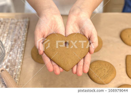 Process of making heart-shaped gingerbread for Valentine's Day. Cutting hearts out of dough with cookie-cutters. Dough, rolling pin and cookie cutters on table. Process of making heart-shaped gingerbread for Valentine's Day. Cutting hearts out of dough with cookie-cutters. Dough, rolling pin and cookie cutters on table. 108979044