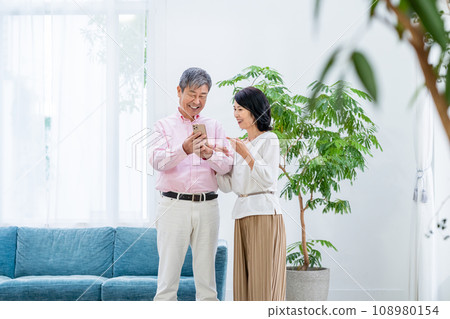 Senior couple with smartphones in the living room 108980154