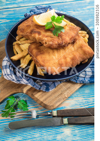 A piece of fried cod with fries on a plate. A piece of fried cod with fries on a plate. 108982316