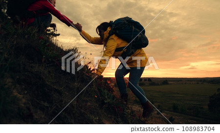Tired woman with backpack climbs on hill top with friend help in autumn park Tired woman with backpack climbs on hill top with friend help in autumn park 108983704