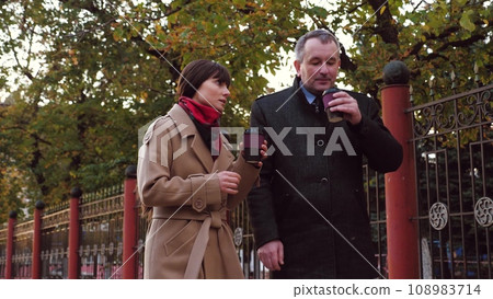 Colleagues discuss company progress drinking hot coffee at meeting in park Colleagues discuss company progress drinking hot coffee at meeting in park 108983714
