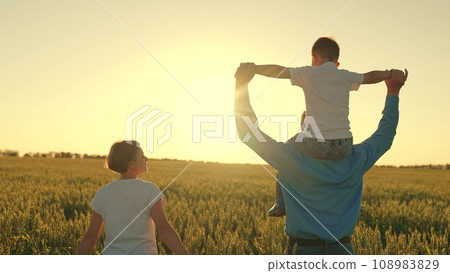 father mother child son happy family. happy family walking at sunset in wheat field. walk journey child boy on dad's shoulders. child surpergero dreams of flying. the dream of a little kid pilot 108983829