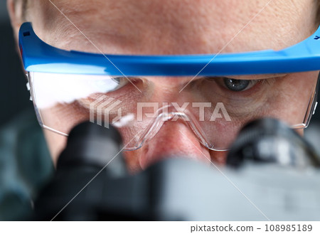 Male laboratory worker eyes looking at microscope wearing goggles 108985189
