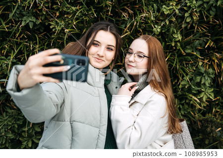 Gen Z influence on the development and popularity of short-form video content on social media platforms. Two girl friends share a moment over smartphone and record video outdoors 108985953