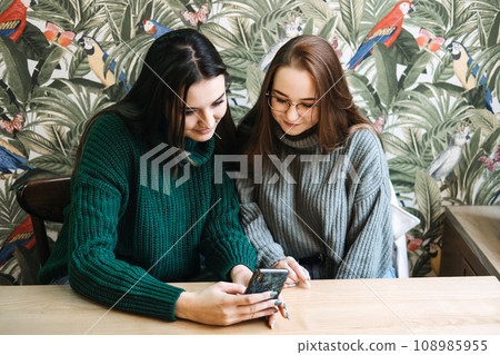 Gen Z influence on the development and popularity of short-form video content on social media platforms. Two girlfriend in cozy sweaters share a moment over smartphone and record video Gen Z influence on the development and popularity of short-form video content on social media platforms. Two girlfriend in cozy sweaters share a moment over smartphone and record video 108985955