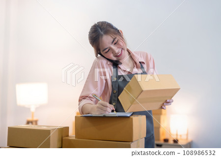 Young woman working online ecommerce shopping at her shop. Young woman sell prepare parcel box of product for deliver to customer. Online selling, ecommerce. Selling products online Young woman working online ecommerce shopping at her shop. Young woman sell prepare parcel box of product for deliver to customer. Online selling, ecommerce. Selling products online 108986532