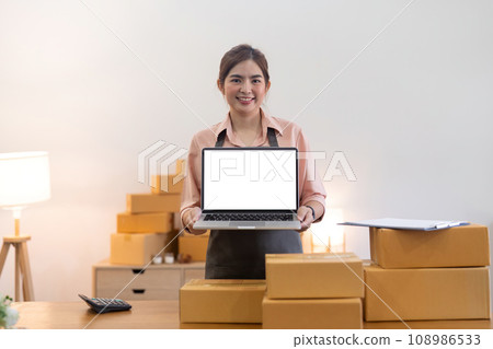 Small business entrepreneur SME , working with box at home, Online sell, ecommerce. mockup of white empty display laptop with box. Concept of online business Small business entrepreneur SME , working with box at home, Online sell, ecommerce. mockup of white empty display laptop with box. Concept of online business 108986533