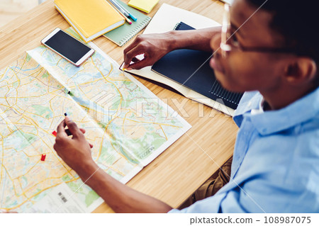 Top view of african american hipster guy pointing on destination on map planning journey vacations Top view of african american hipster guy pointing on destination on map planning journey vacations 108987075