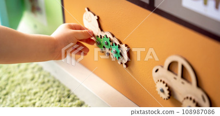 Toddler boy is playing with a busy board. Educational toy for young children. Focus on a wooden caterpillar. Close up 108987086