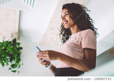 Young smiling female standing with smartphone device in hands 108987310