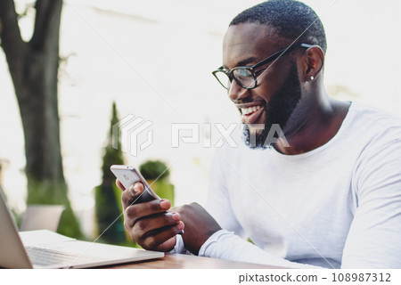 casual dressed young man blogging on mobile phone sitting at street cafe casual dressed young man blogging on mobile phone sitting at street cafe 108987312