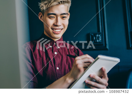 Positive japanese hipster student drawing sketch on notepad sitting in modern space 108987432