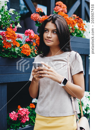 attractive hipster girl holding smartphone connected to 4G internet strolling on spring street 108987438