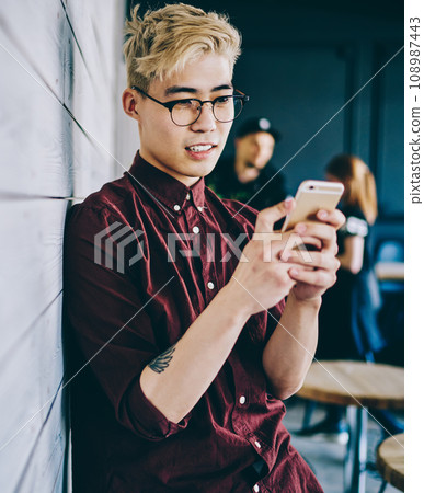 Asian young man chatting online on mobile phone Asian young man chatting online on mobile phone 108987443