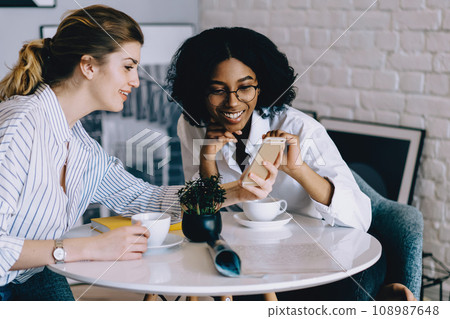 Positive two multicultural young women dressed in casual wear watching funny video in internet blog 108987648