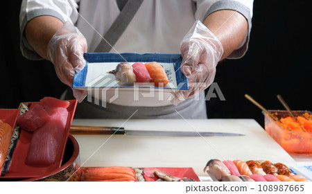 A skilled sushi chef proudly presenting a beautifully arranged plate of delicious sushi, demonstrating the artistry and precision involved in the culinary world. A skilled sushi chef proudly presenting a beautifully arranged plate of delicious sushi, demonstrating the artistry and precision involved in the culinary world. 108987665