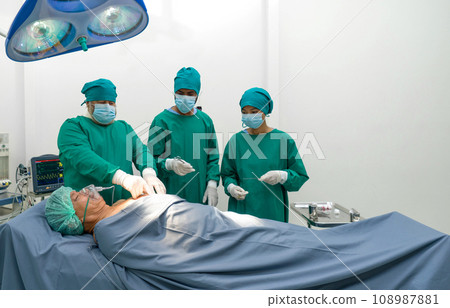 Group of surgeons, steeped in concentration, performing complex surgery in operating room. Sterile surgical instruments pepper the surrounding space, while monitors display vital patient data. 108987881