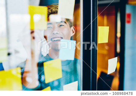 Cheerful asian hipster guy satisfied with using colorful stickers during learning and prepare homework Cheerful asian hipster guy satisfied with using colorful stickers during learning and prepare homework 108988478