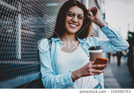 Positive hipster girl with modern cellular standing on street Positive hipster girl with modern cellular standing on street 108988763