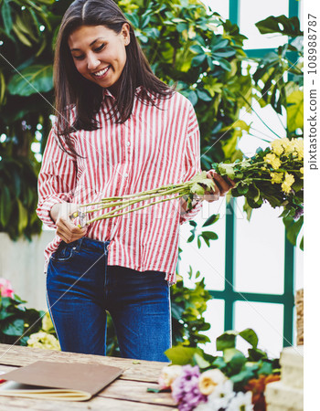 Cheerful asian woman designing floral composition while working in glasshouse near desk 108988787