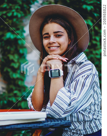 Portrait of cheerful caucasian female student with wristwatch on hand sitting at table in cafe outdoors 108988822