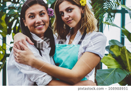 prosperous female proprietors of orangery in apron looking at camera and embracing 108988931